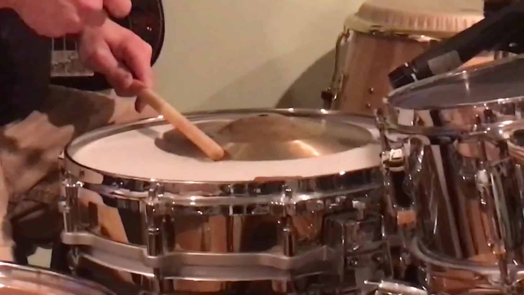 snare drum with splash cymbal on batter head being struck with a drum stick